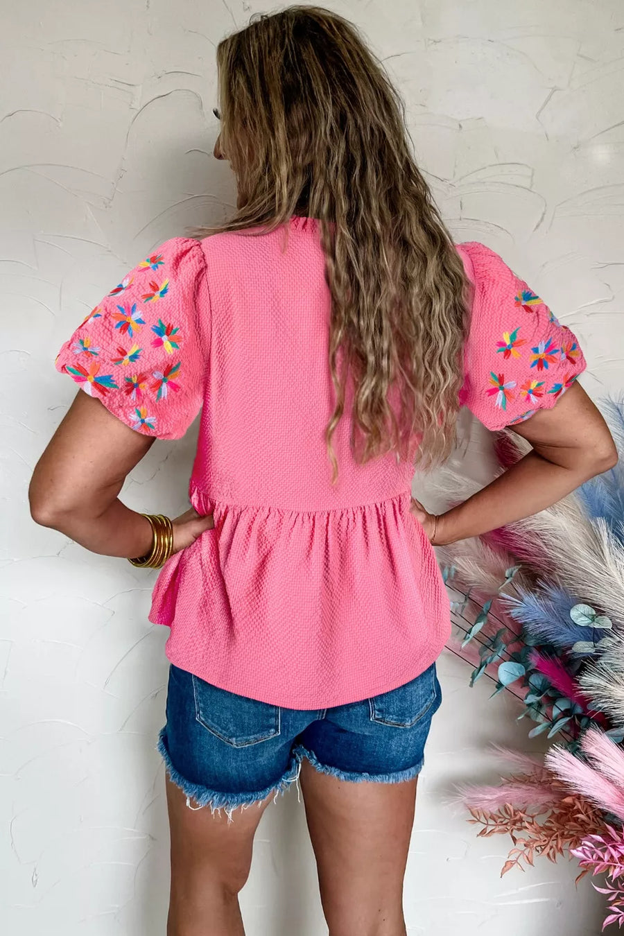 Women's pink textured peplum blouse with embroidered floral puff sleeves.