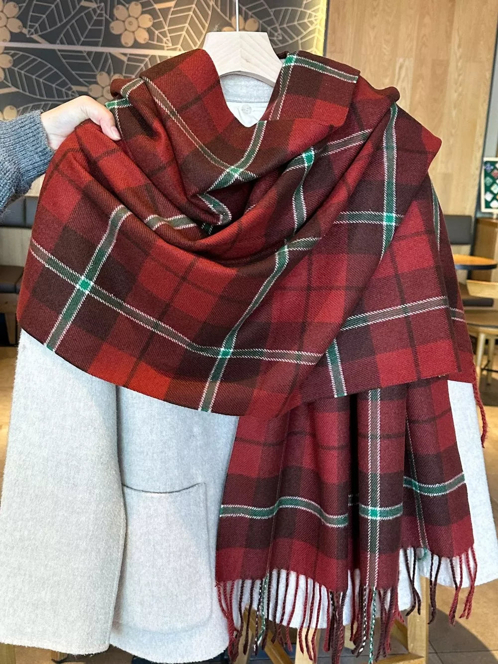 Red plaid fringe scarf with green and white accents, draped over a light grey coat.