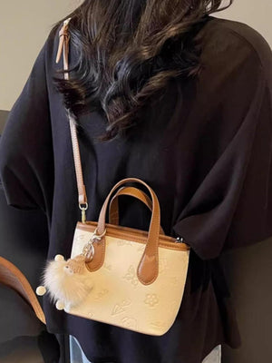 Mini crossbody bag in cream embossed PU leather with brown trim and a fluffy charm.