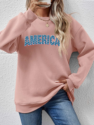 Blush pink crewneck sweatshirt with "AMERICA" graphic in blue and white stars.
