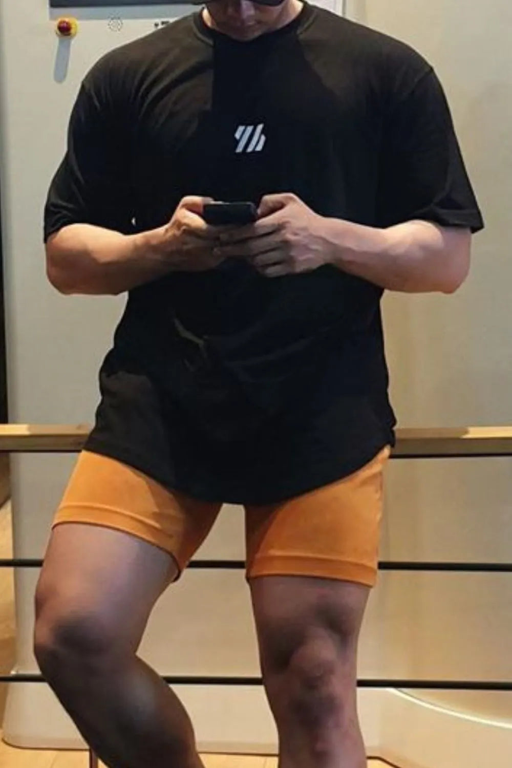 Black oversized tee with white logo detail, paired with orange shorts.