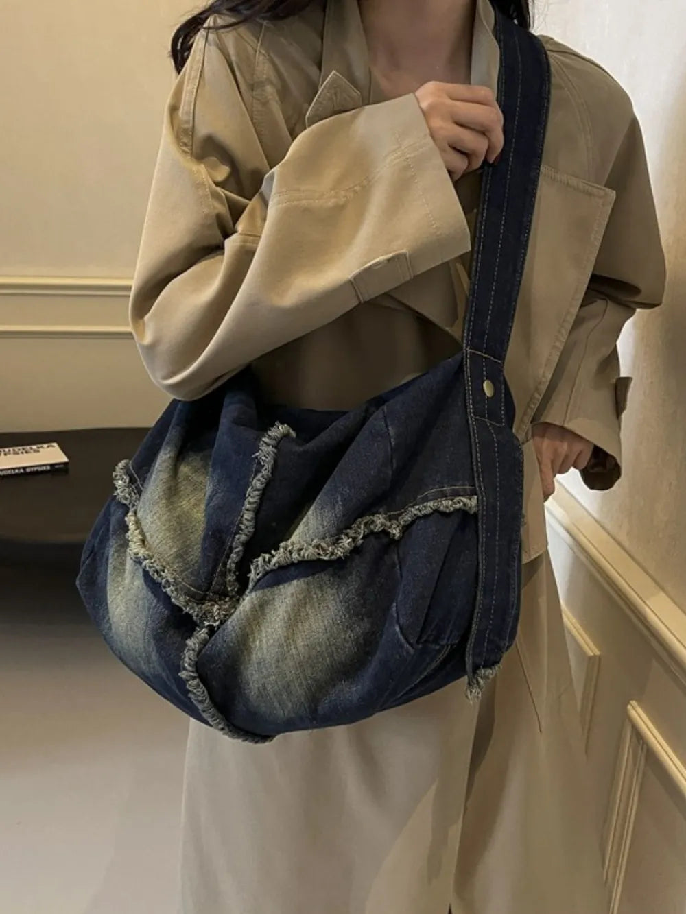 Frayed denim slouch crossbody bag in dark wash with distressed details and a single strap.