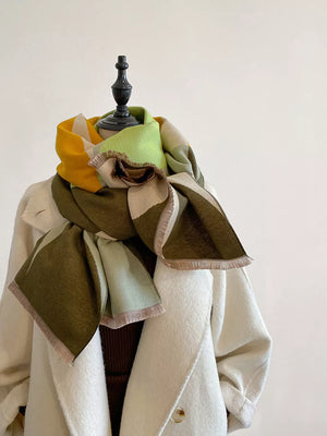 Soft geometric patterned scarf with fringes in green, yellow, and beige tones.
