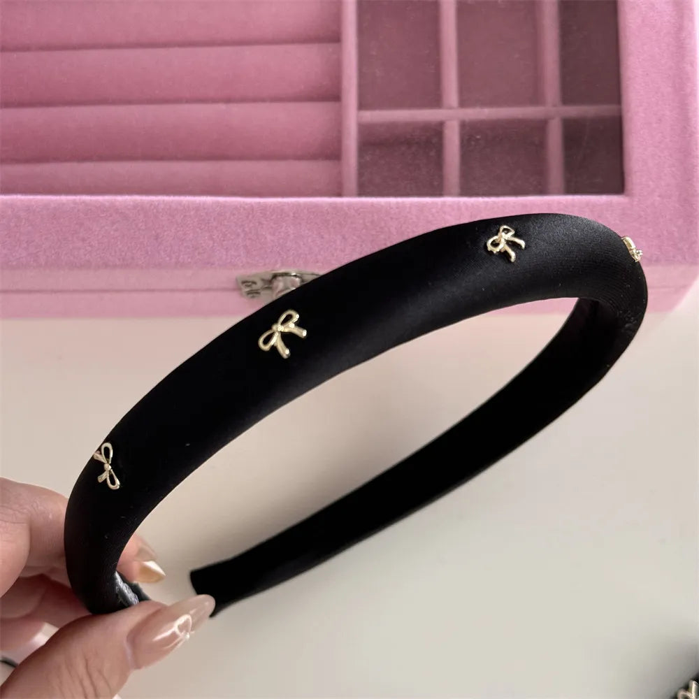 Black padded satin headband with gold bow embellishments.