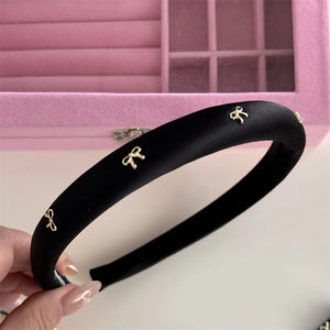 Black padded satin headband with gold bow embellishments.
