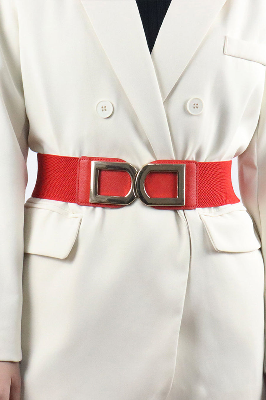 Red elastic belt with double gold buckle detail worn over a white blazer