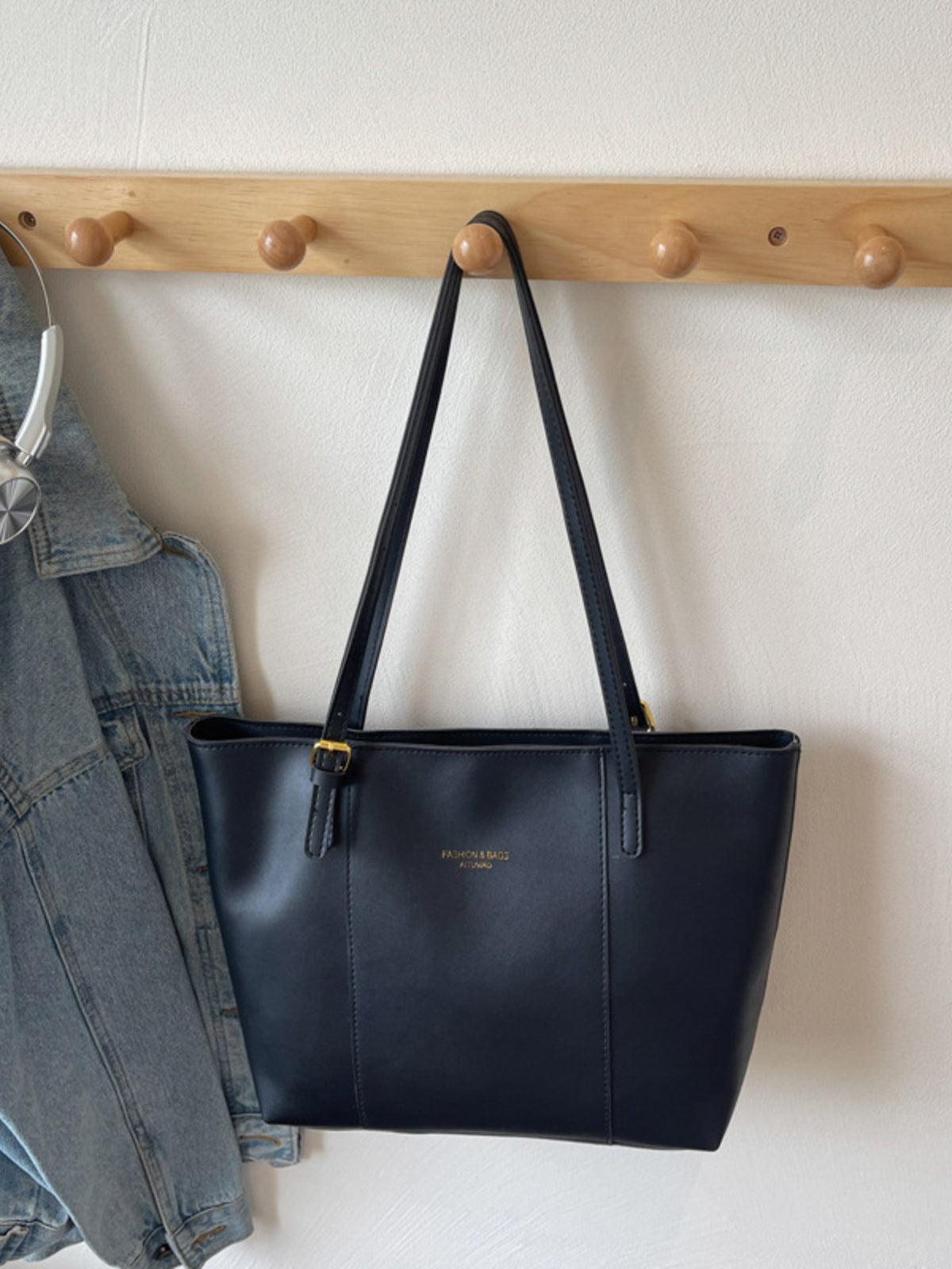 Black structured tote bag made of PU leather with gold buckle detail and gold embossed logo.