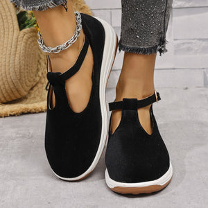 Black T-bar flat slip-ons with adjustable ankle strap and white sole.