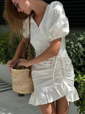 White wrap dress with puff sleeves, V-neck, ruched side detail, and ruffled hem.
