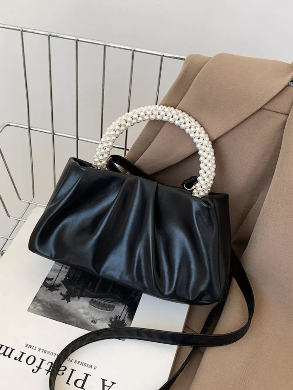 Black ruched crossbody bag with elegant pearl handle and adjustable strap.
