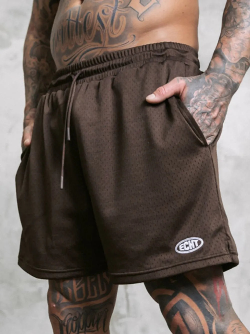 Men's dark brown perforated performance drawstring shorts with pockets and logo detail.