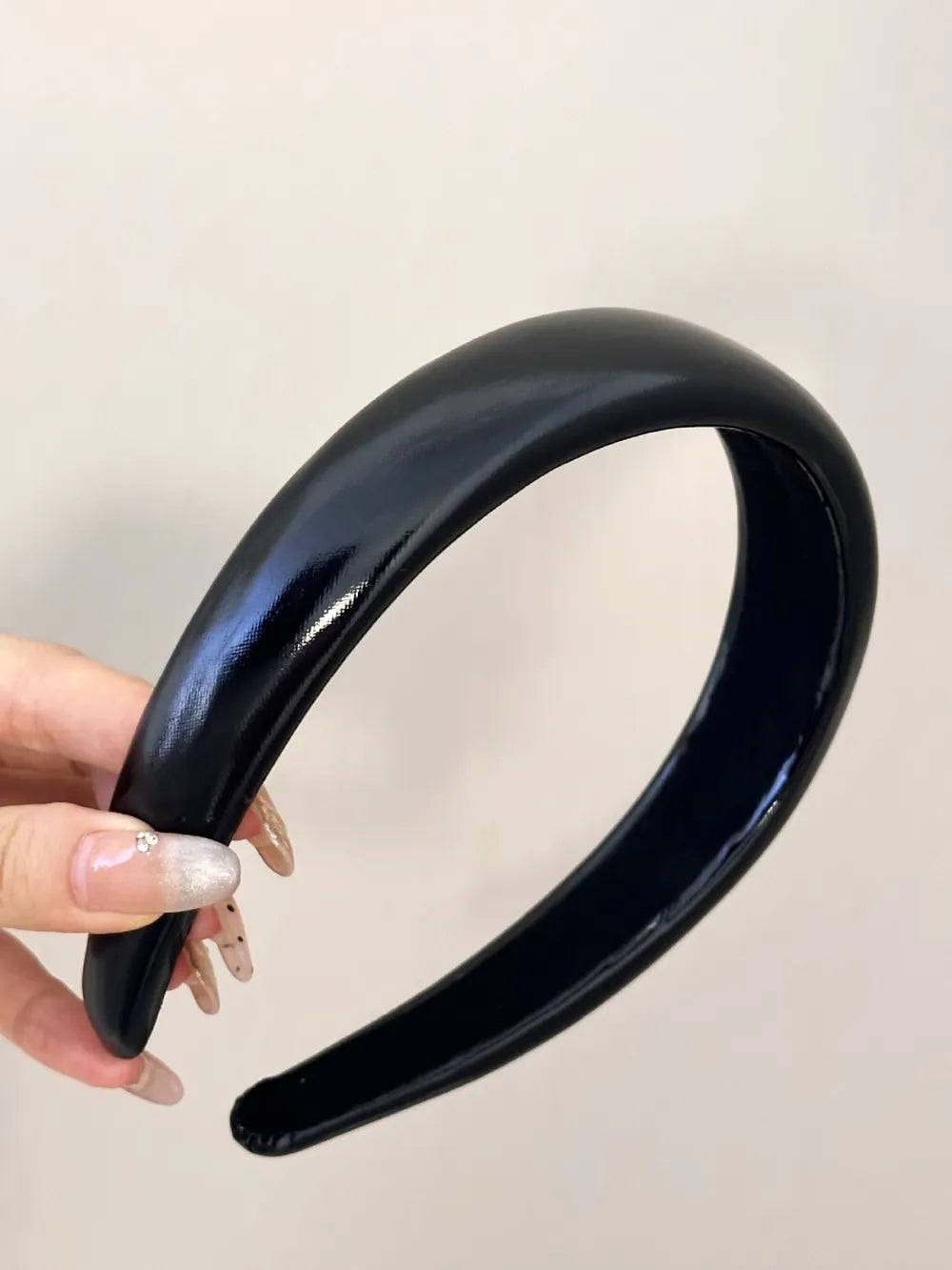 Glossy padded black headband with a smooth, patent-like finish.