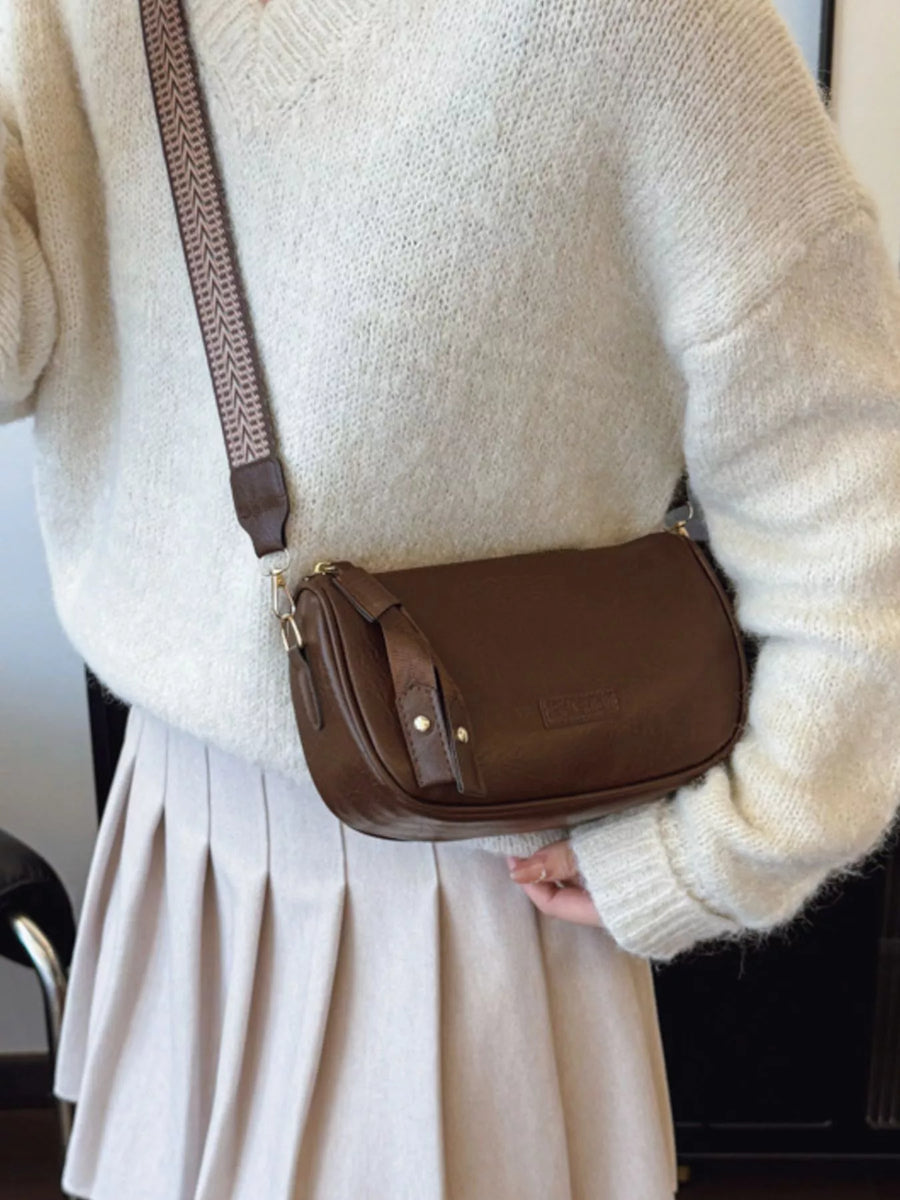 Brown leather crossbody bag with patterned strap and gold hardware detail.