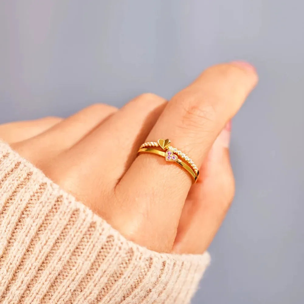 Gold layered rings with heart details and small stones on a finger.