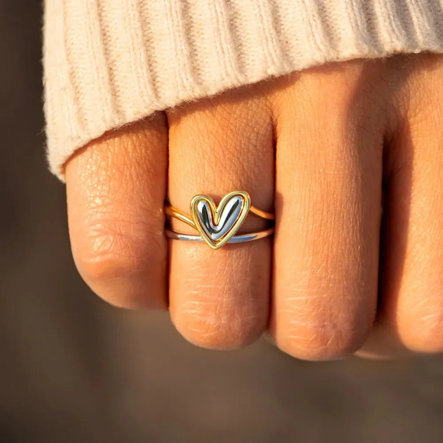 Two-tone gold heart outline ring stacked with a silver band.