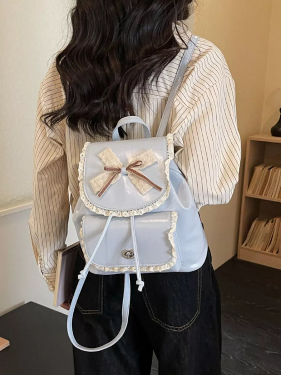 Blue mini backpack with lace trim, bow, and buckle closure.