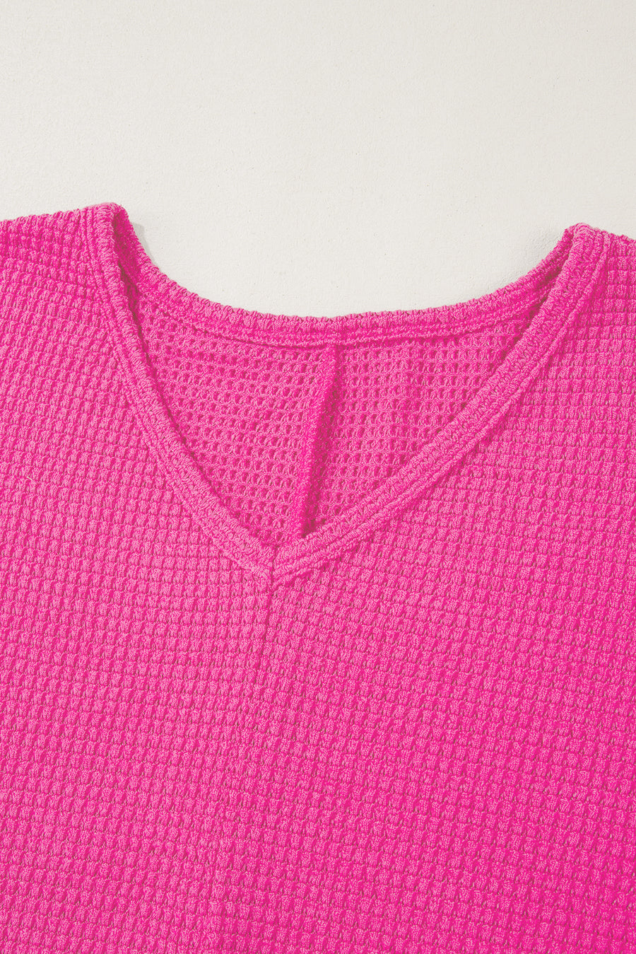 Hot pink waffle knit V-neck top with a slit hem detail.