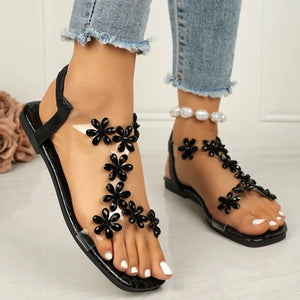 Black PVC floral embellished flat sandals with clear straps.