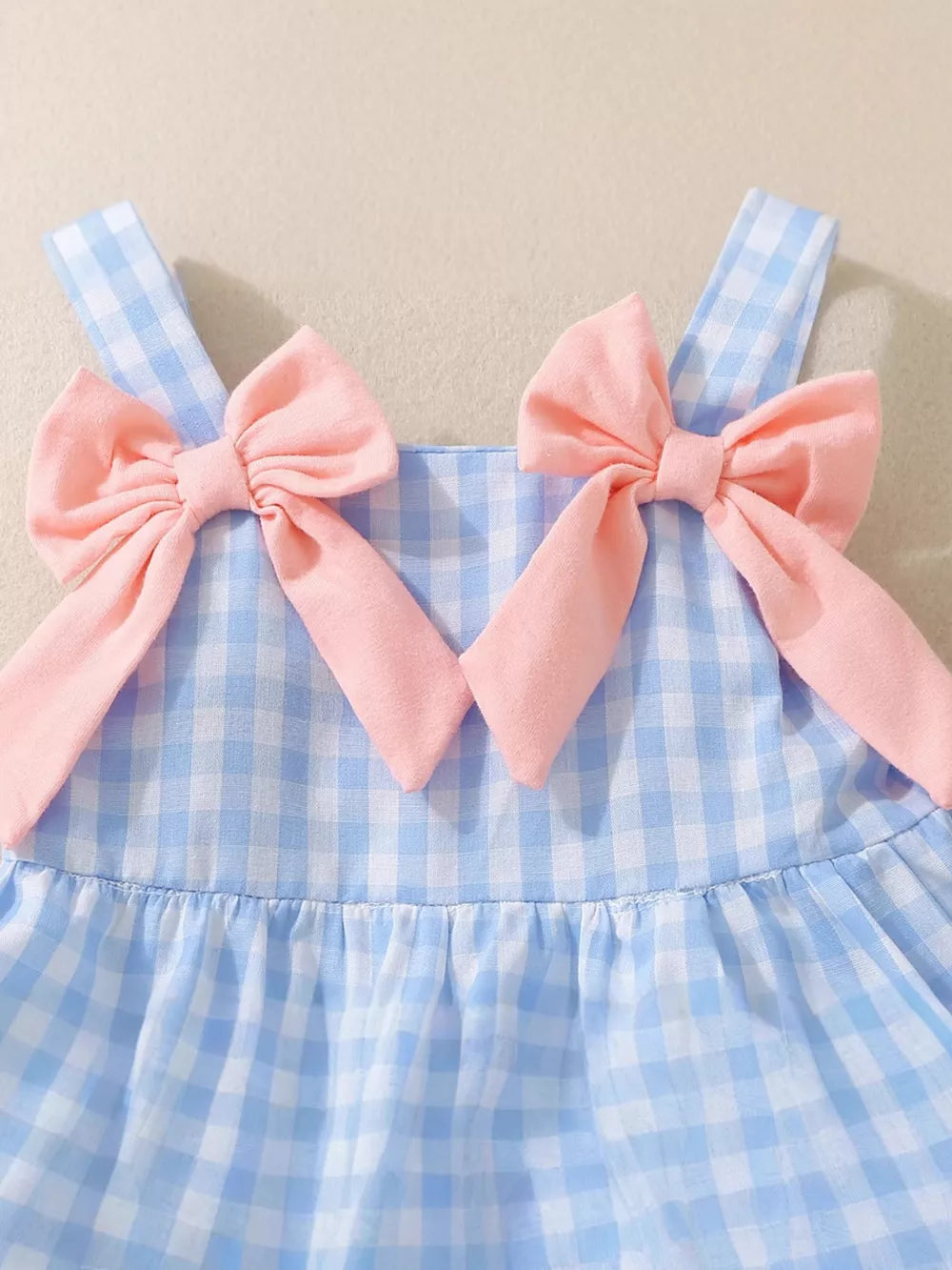 Blue gingham baby dress with pink bow shoulder straps and ruffled skirt.