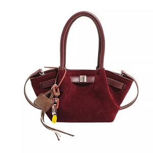 Burgundy suede and leather mini tote bag with metal clasp and charm detail.