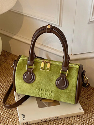 Green barrel crossbody bag with brown trim and handles, gold zippers, and embossed text detail.