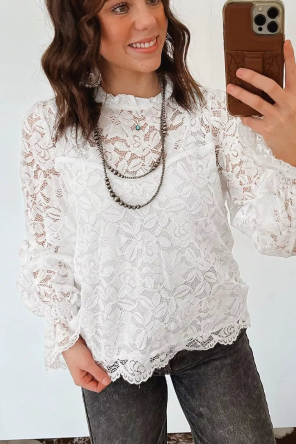 White lace blouse with ruffled neckline, long sleeves, and scalloped hem.
