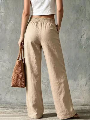 Beige linen wide-leg pants with elastic waistband and side pockets, styled with a straw bag.
