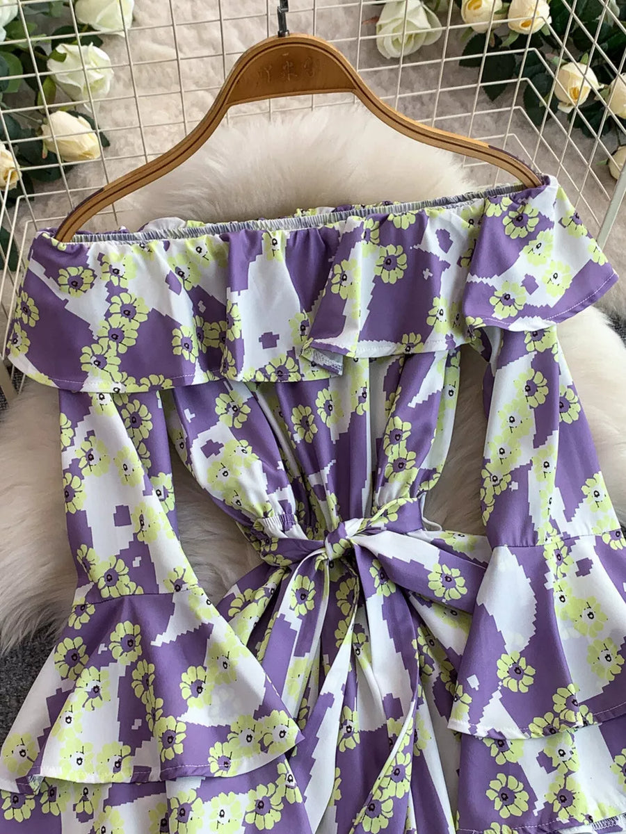 Purple floral off-shoulder ruffled romper with tie waist and bell sleeves.
