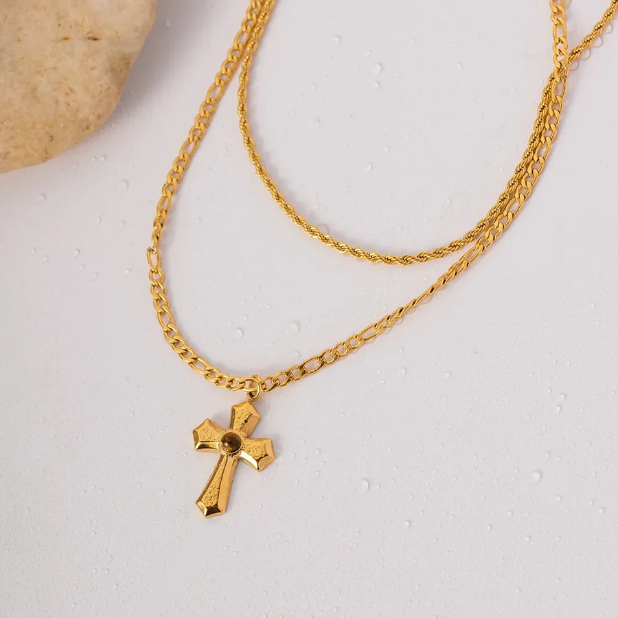 Gold layered chain necklace with a sculpted cross pendant featuring a brown stone detail.