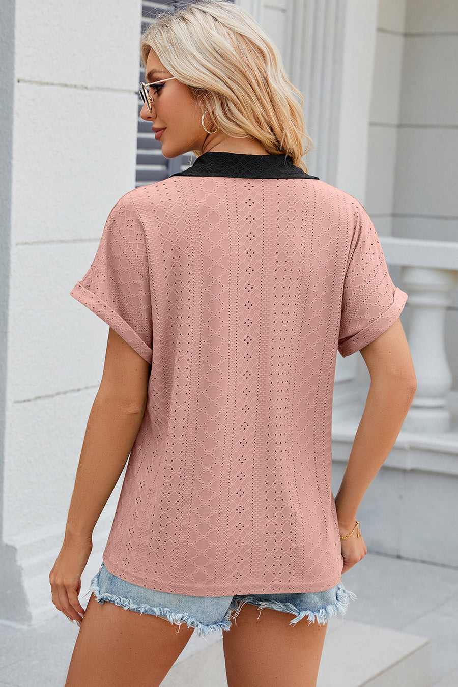 Blush pink perforated polo top with black collar and cuffed short sleeves.