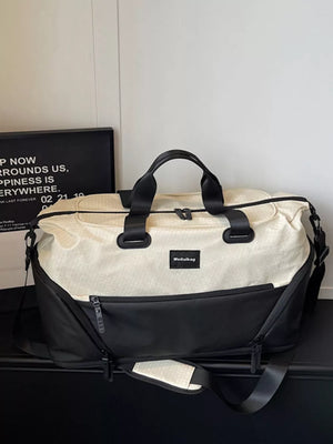 Textured two-tone large duffle bag in cream and black with adjustable strap and zip pockets.