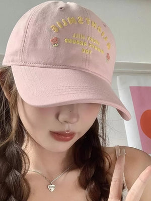 Pink baseball cap with embroidered yellow text and roses.