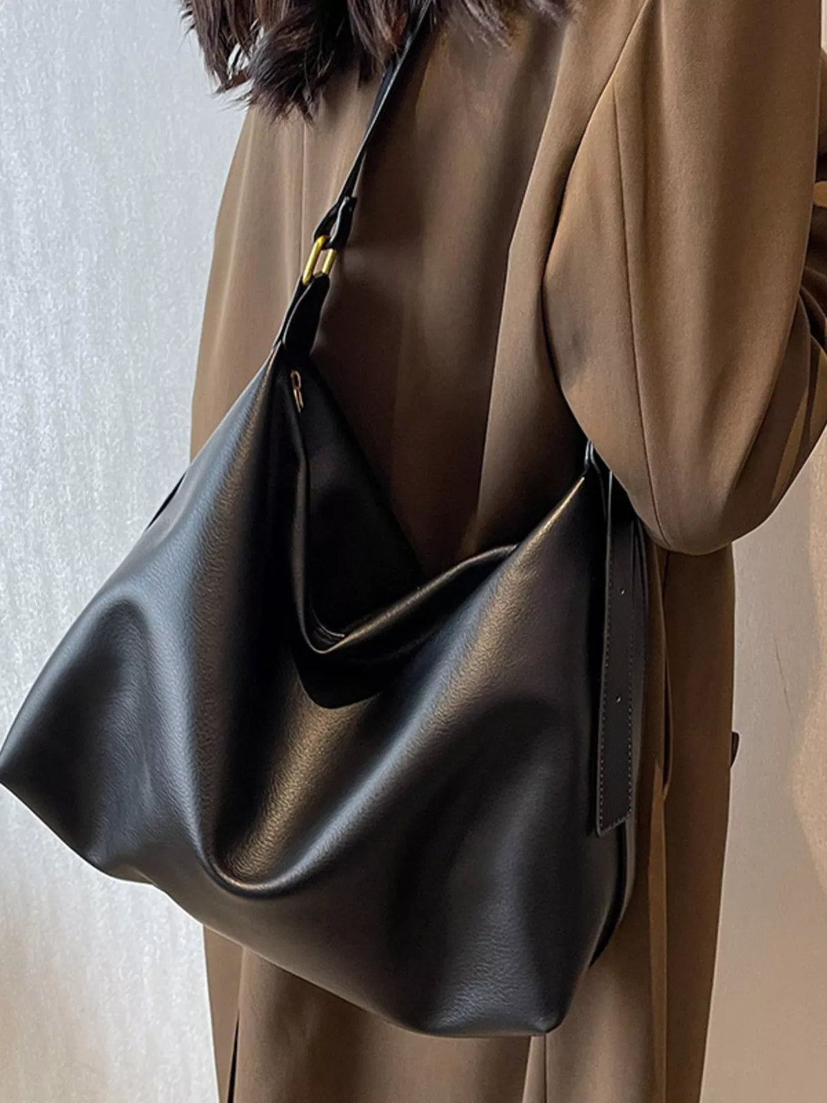 Black sculptural PU leather shoulder bag with adjustable strap and gold hardware detail.