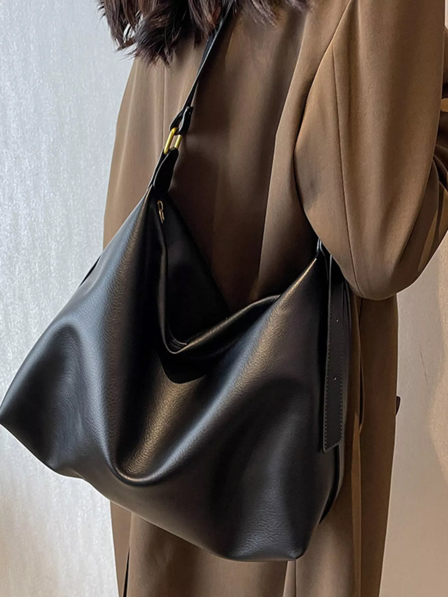 Black sculptural PU leather shoulder bag with adjustable strap and gold hardware detail.