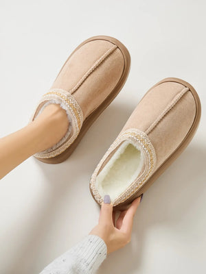 Tan shearling house slippers with embroidered trim and plush lining.