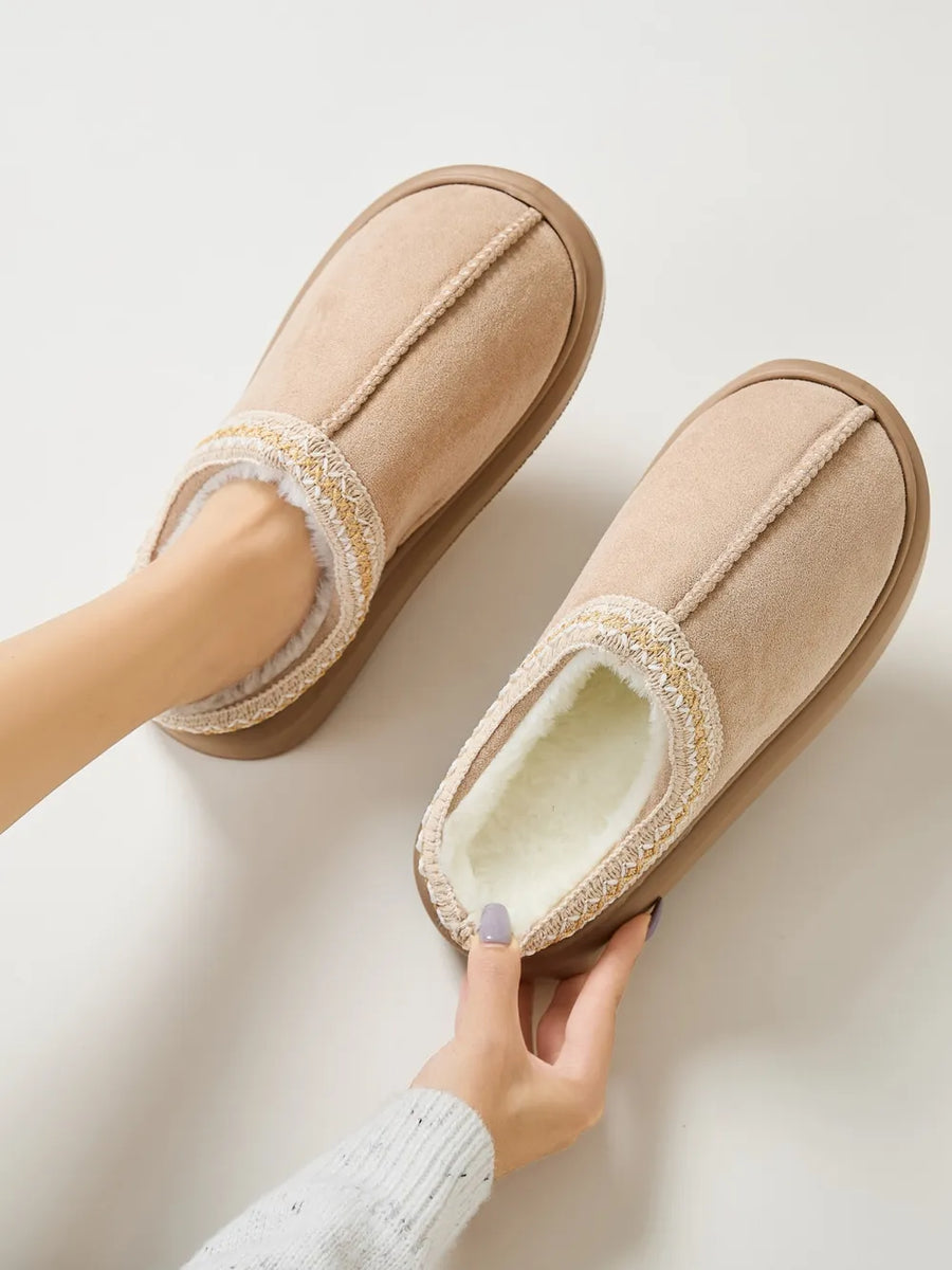 Tan shearling house slippers with embroidered trim and plush lining.