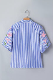 Blue and white striped button-down blouse with pink floral embroidery on the sleeves.