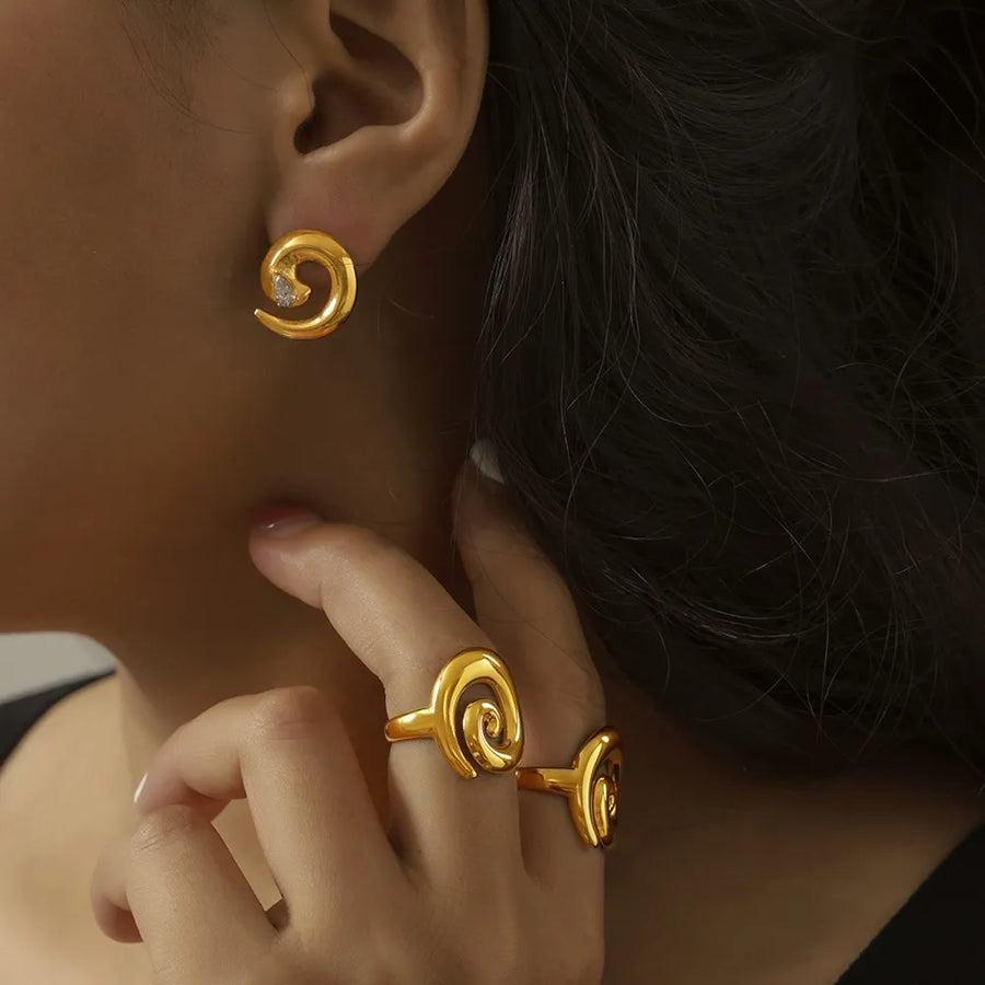 Gold swirl stud earrings with a small zirconia detail and matching swirl ring.
