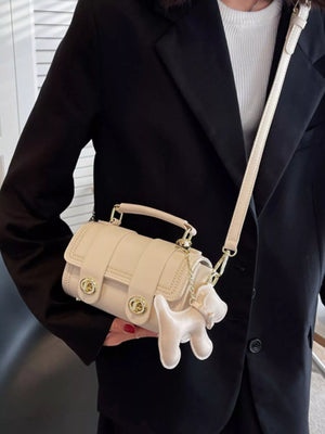 Beige PU leather crossbody bag with dog charm and gold hardware, styled with a black blazer.