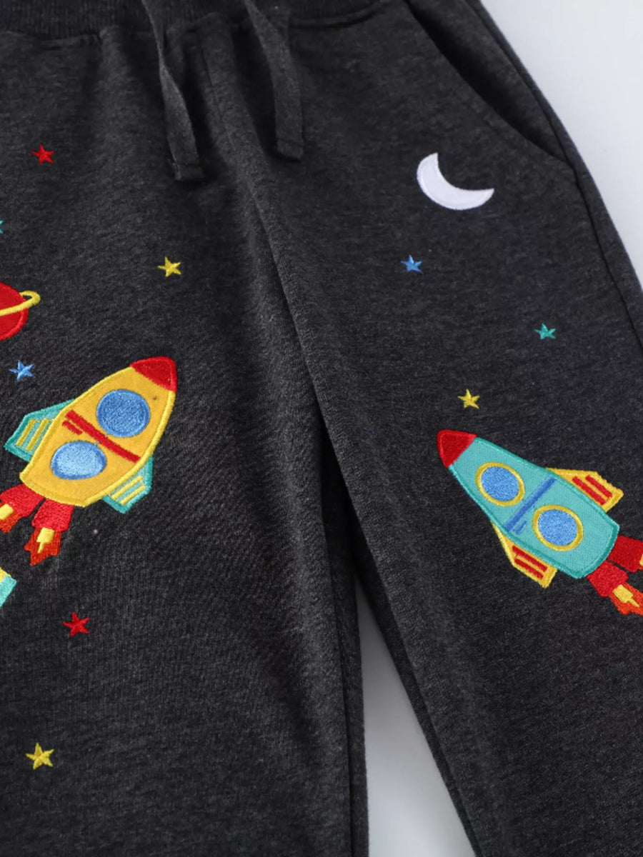 Black cotton blend joggers for kids with embroidered rockets, stars, and a moon.