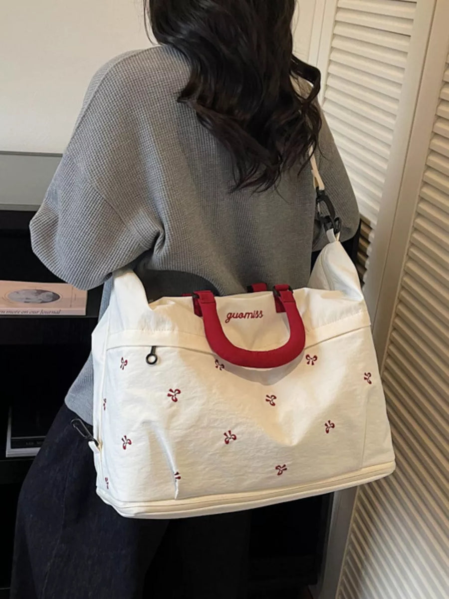 White tote bag with red bow pattern and red handles, embroidered logo.