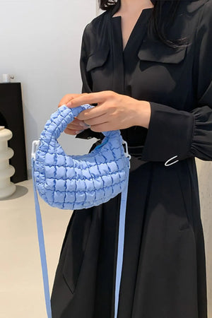 Padded crescent crossbody bag in pastel blue with quilted texture and white hardware.