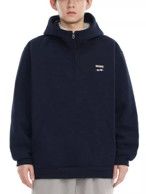 Navy blue quarter-zip hoodie with a small embroidered patch that says "BELIEVE IN ME".