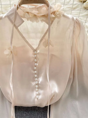 Apricot sheer organza shirt with floral appliqué, pearl buttons, and tie neck.