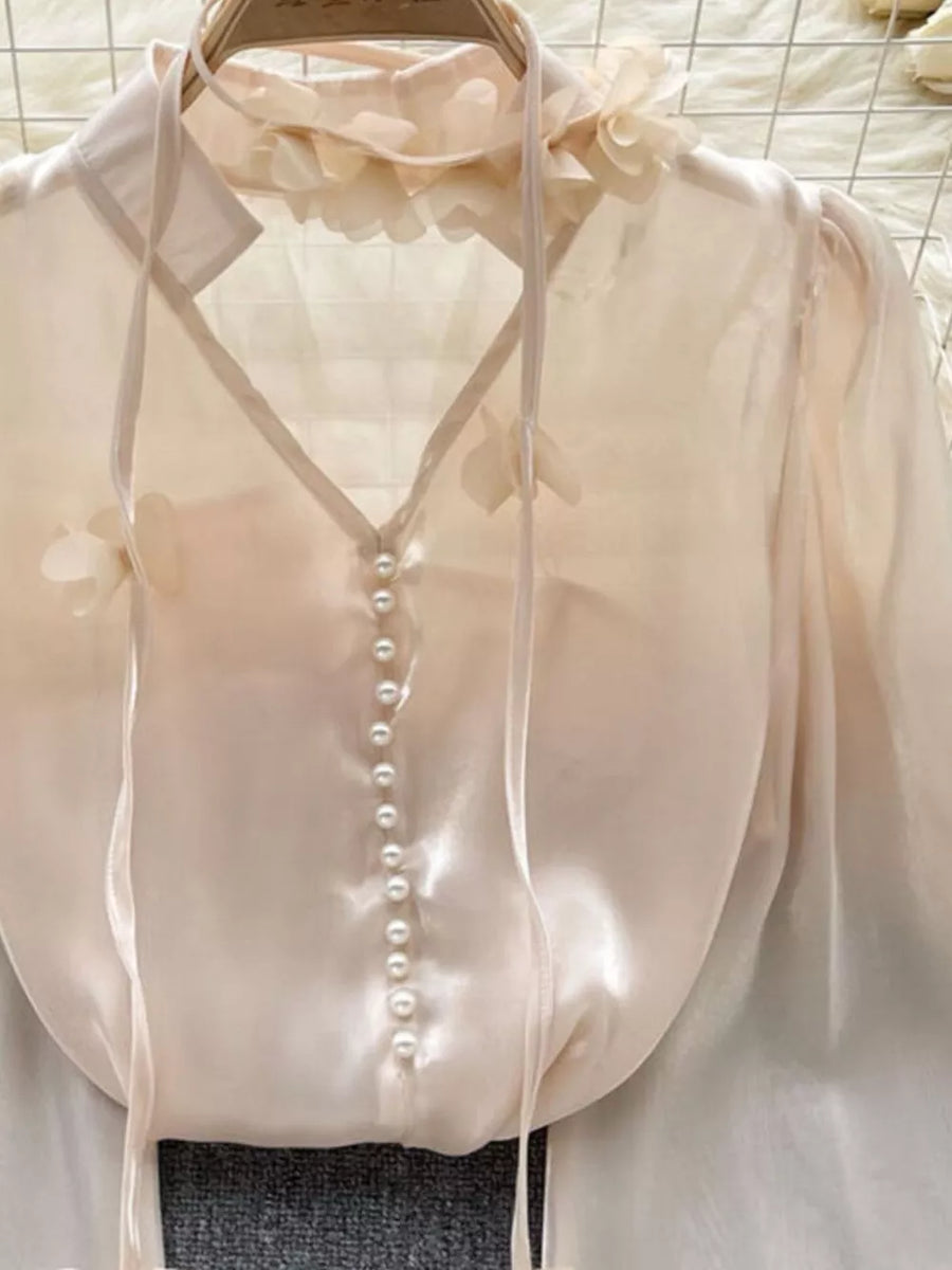 Apricot sheer organza shirt with floral appliqué, pearl buttons, and tie neck.
