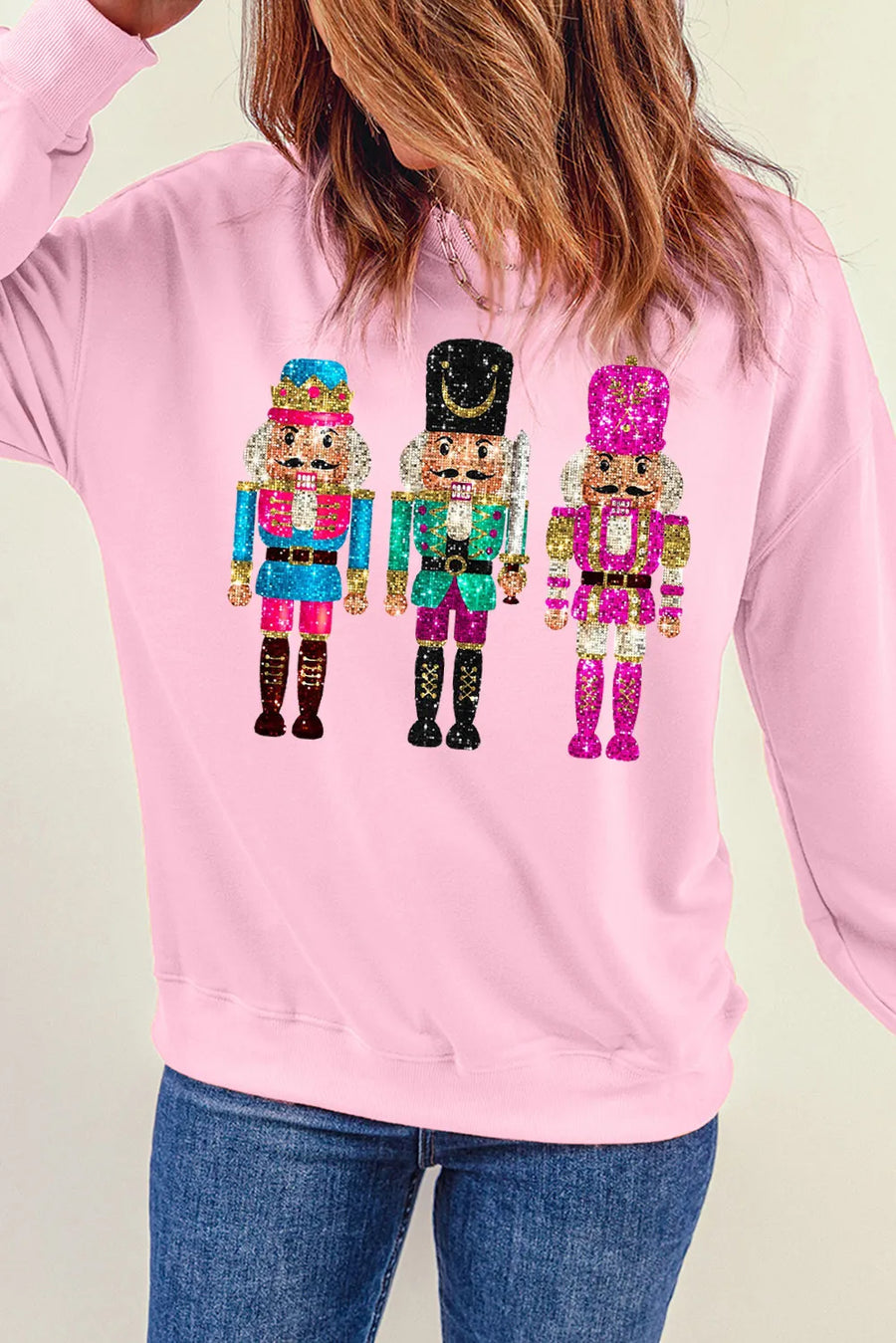 Blush pink crewneck sweatshirt with a graphic of three sequined nutcrackers.