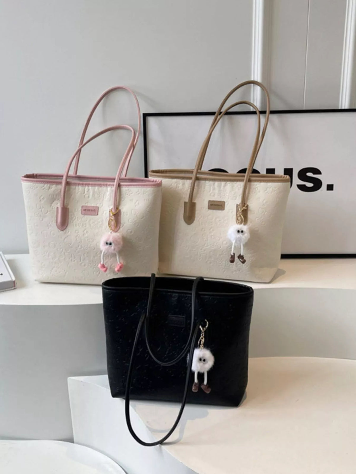 Embossed PU leather tote bag in black, pink, and khakis with charm details.