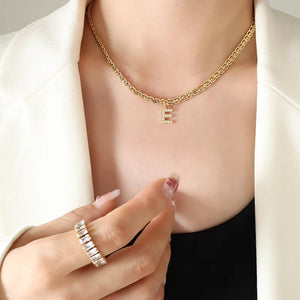 Gold chain necklace with a zircon-set initial E pendant, styled with a ring.