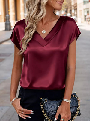 Wine red satin V-neck blouse with short sleeves, styled with a necklace and black pants.