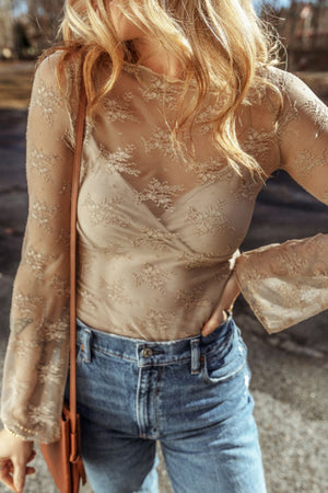 Floral lace wrap bodysuit in tan with bell sleeves, worn with jeans.